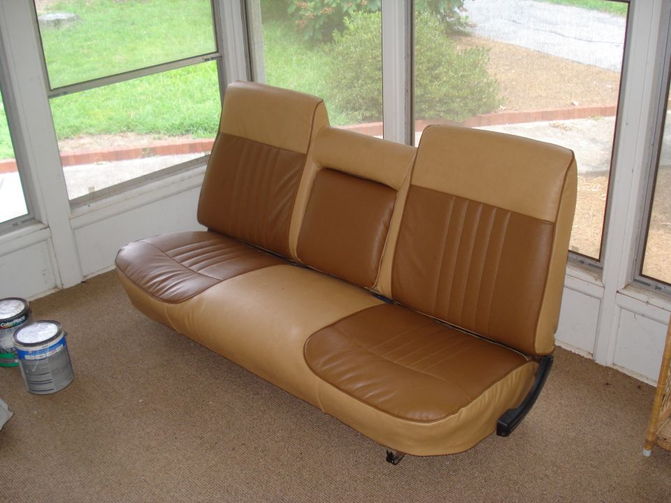 Two-tone tan and brown vinyl bench seat with a center armrest, sitting on carpet