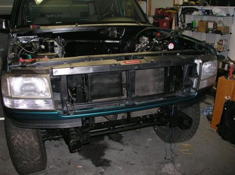 1996 Ford Bronco - The front end of a green SUV is shown with the hood open, revealing the engine compartment and radiator.