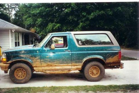 1996 Ford Bronco - This teal Ford Bronco is covered in mud, indicating recent off-road use.
