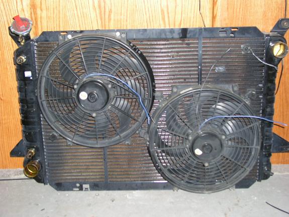 Radiator assembly with two black electric fans and blue wiring. Red cap on top left