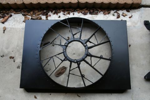 1996 Ford Bronco - A black radiator fan shroud is shown, a large, multi-bladed fan assembly. The part is resting on a concrete surface.