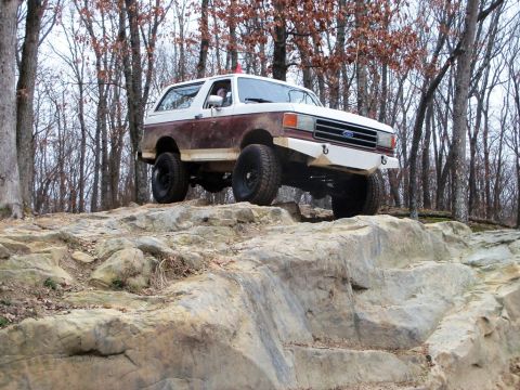 1989 Ford Bronco - Ford Bronco navigates a rocky trail in a wooded area.