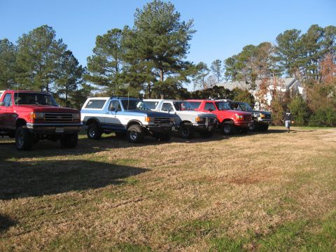 1994 Ford Bronco - A lineup of SUVs and trucks are parked on a dry, grassy field under a clear blue sky.
