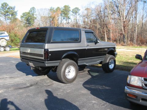 1994 Ford Bronco - A two-tone Ford Bronco with aftermarket wheels and tires is parked outdoors next to a red pickup truck.