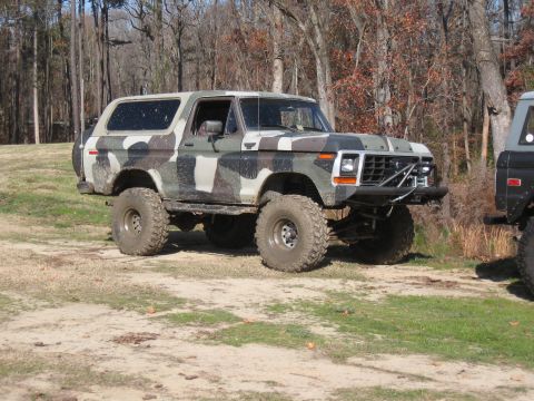 1994 Ford Bronco - A lifted, camouflaged Ford Bronco sits on a dirt lot next to another vehicle.