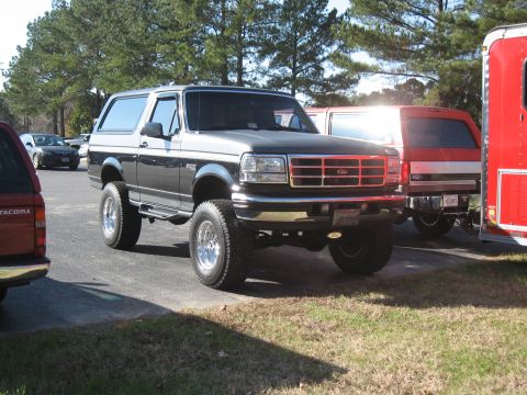 1994 Ford Bronco - This lifted Ford Bronco is parked outdoors next to other vehicles and a trailer.
