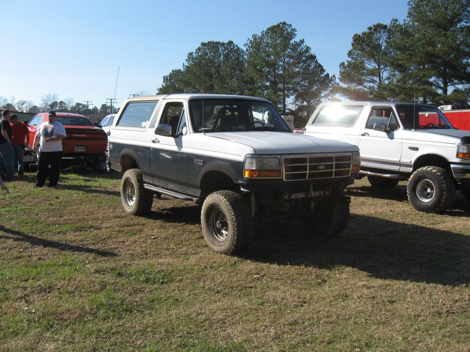 Lifted two-tone Ford Bronco and white Ford F-Series truck parked on grass