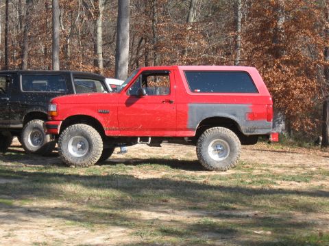 1994 Ford Bronco - A red Ford Bronco with off-road tires is parked outdoors next to another SUV.