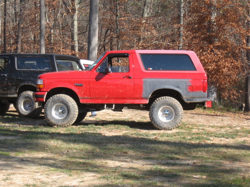 Side view of red Ford Bronco with large tires, parked next to a black SUV