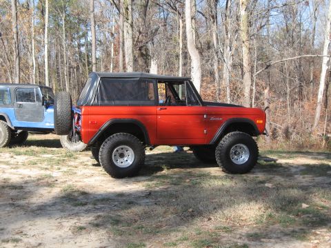 1994 Ford Bronco - An orange Ford Bronco is parked next to a blue Jeep in a wooded area.