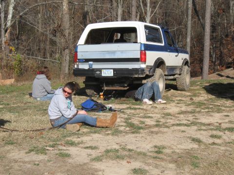 1994 Ford Bronco - A 1994 Ford Bronco is parked outdoors with people relaxing around it, one person working underneath.