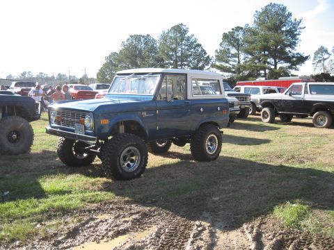 1994 Ford Bronco - Modified blue Ford Bronco with a white top and lifted suspension sits in a muddy field.