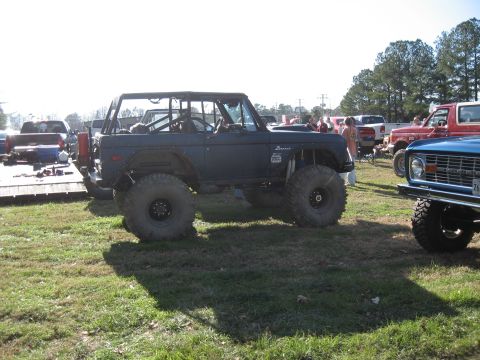 1994 Ford Bronco - This modified Ford Bronco features a roll cage and oversized tires, parked outdoors with other vehicles nearby.