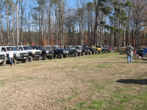 1994 Ford Bronco - A row of Ford Broncos are parked on a grassy field, with a man standing near the front of the line.