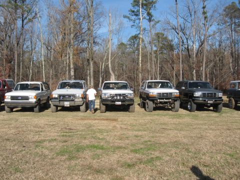 1994 Ford Bronco - A lineup of SUVs are parked in a field on a clear day, with a person walking between them.