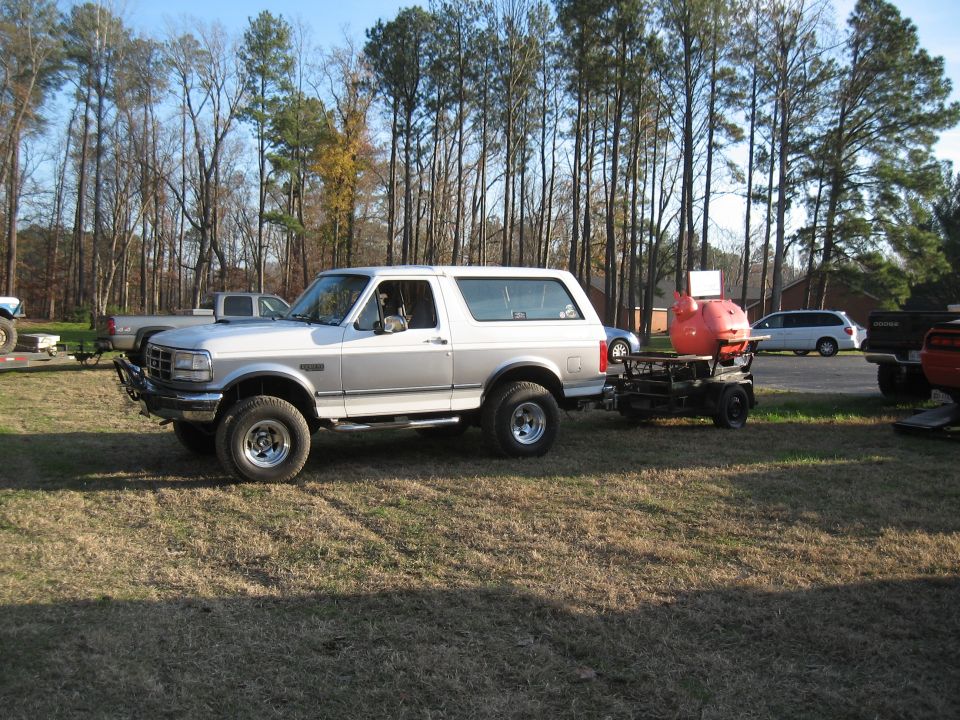 1994 Ford Bronco side view, towing a trailer with an orange grill