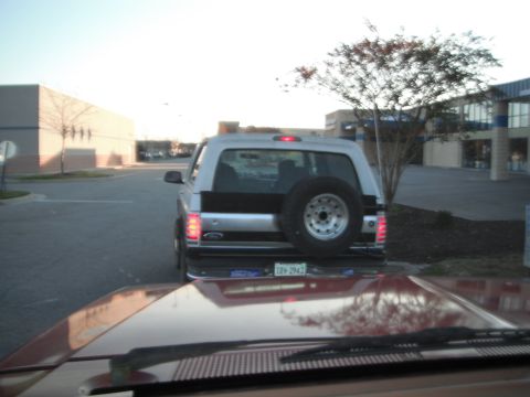 1989 Ford Bronco - The rear of a silver and black Ford Bronco is seen from another vehicle's perspective, parked in a lot.