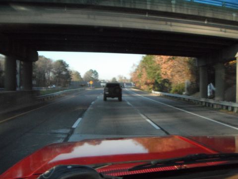 1989 Ford Bronco - A dark-colored SUV is seen from behind on a highway, traveling under a concrete overpass.
