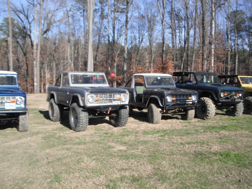 Several Ford Broncos parked in a grassy field. The closest one is gray with a black hood and large tires