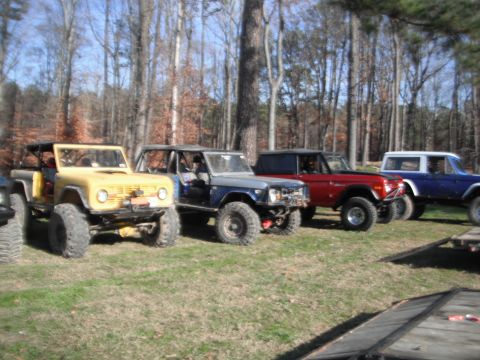 1989 Ford Bronco - Several off-road vehicles, including a yellow Ford Bronco, are parked in a wooded area.