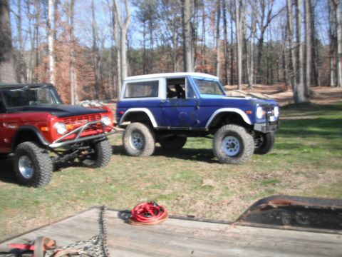 1989 Ford Bronco - Two Ford Broncos, one red and one blue, are parked outdoors in a grassy, wooded area.