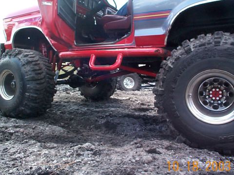 1992 Ford Bronco - Modified off-road truck with large tires and red roll cage, another vehicle visible in background.