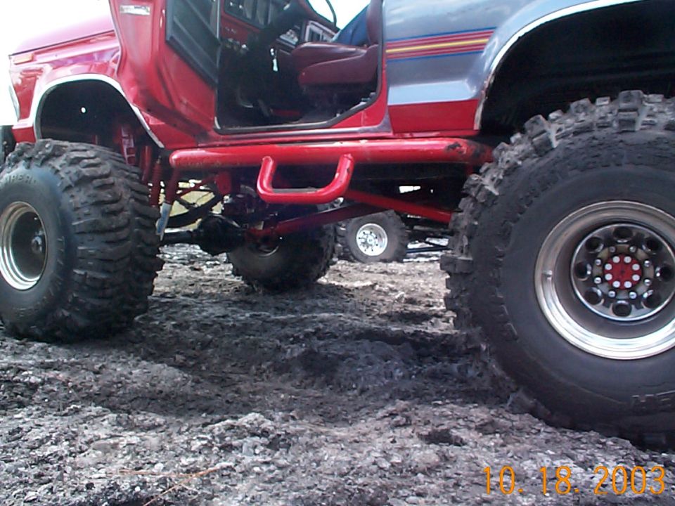 Lifted red and silver Ford with doors off on giant Super Swamper mud tires, low side view in mud