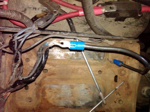 1988 Ford Bronco - Close-up of vehicle battery cables and terminals attached to a rusty bracket.
