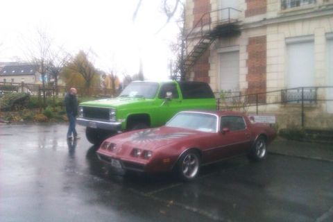 1991 Ford LTD Crown Victoria - A red Pontiac Firebird and a green Chevy K5 Blazer are parked outside a brick building on a wet day.