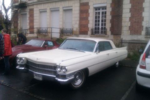 1991 Ford LTD Crown Victoria - A white 1963 Cadillac sedan is parked next to a red car and a modern vehicle.