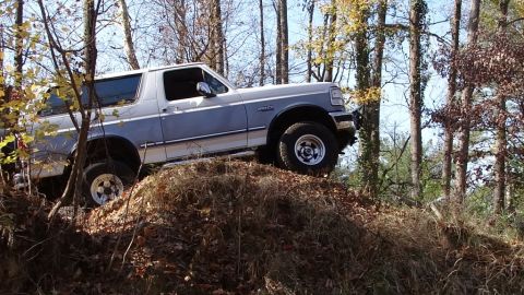 1994 Ford Bronco - 1994 Ford Bronco navigates an off-road trail through a forest during autumn.