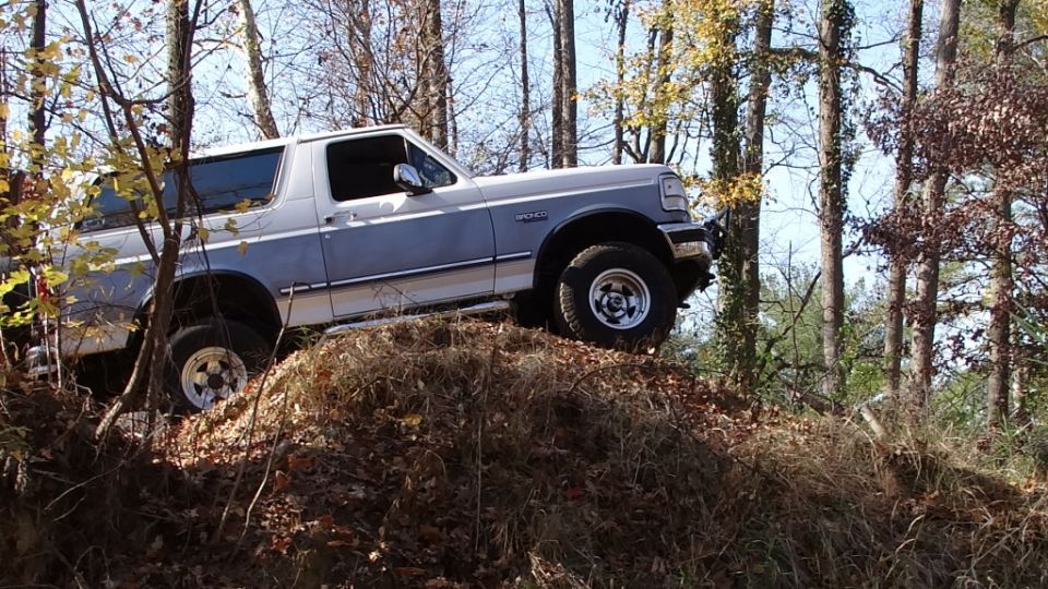 1994 Ford Bronco climbing a dirt mound in a wooded area