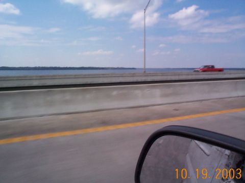 1992 Ford Bronco - A red pickup truck drives across a bridge with a large body of water to the left.