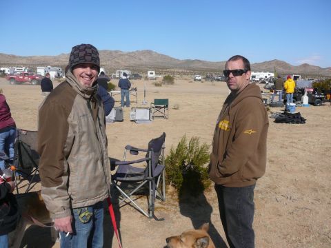 1988 Ford Bronco - A desert campsite scene with two men, a dog, and various vehicles and RVs in the background.