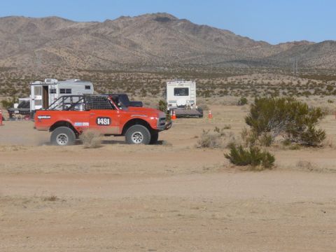 1988 Ford Bronco - An off-road vehicle races through a desert landscape, with RVs and mountains in the background.