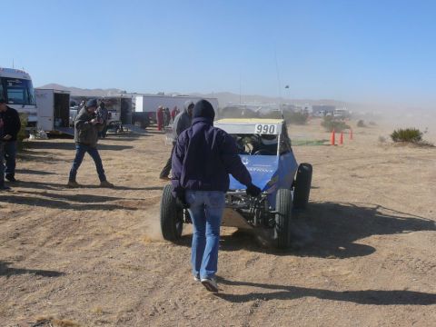 1988 Ford Bronco - A blue off-road buggy, marked with the number 990, is seen in a dusty desert environment with other vehicles and people present.