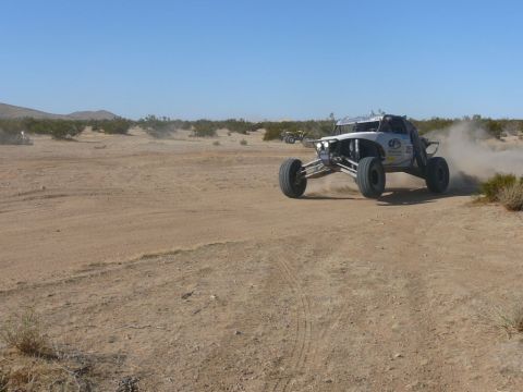 1988 Ford Bronco - Off-road buggy navigates a dusty desert terrain under a clear blue sky.