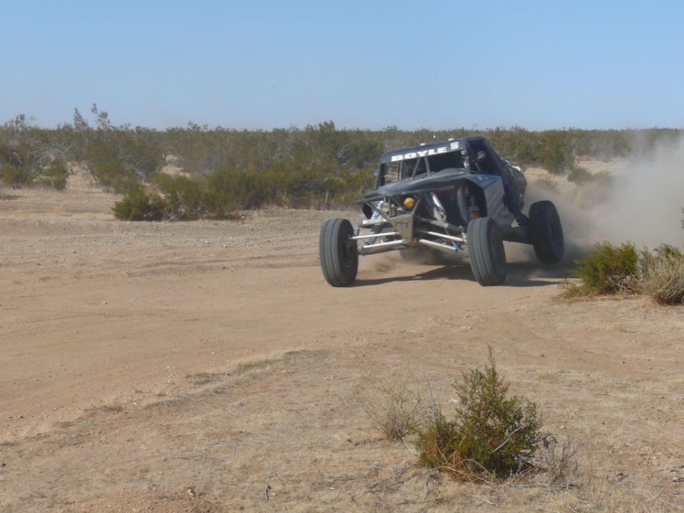 Buggy kicking up dust on a dirt track with desert brush