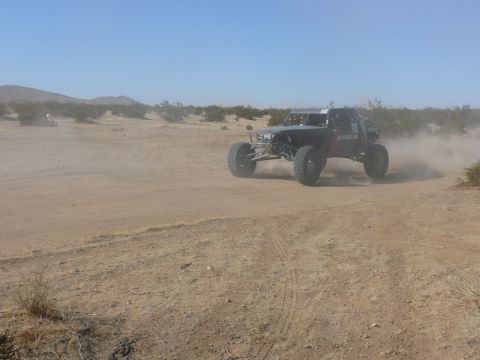 1988 Ford Bronco - A custom off-road buggy navigates a dusty desert terrain under a clear blue sky.