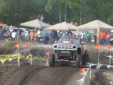 1994 Ford Bronco - A lifted pickup truck navigates a muddy course with spectators in the background.