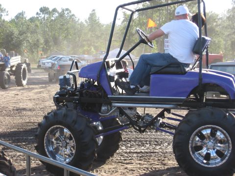1994 Ford Bronco - A modified golf cart with large tires is seen at an outdoor event with other vehicles in the background.