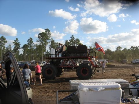 1994 Ford Bronco - Custom monster truck with people riding on top is seen at an outdoor event with other vehicles.