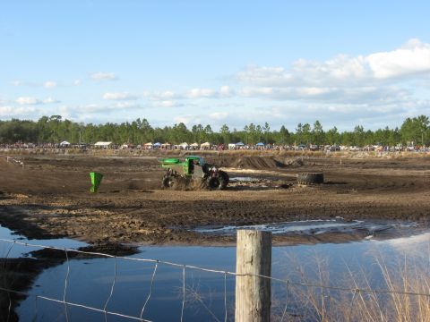 1994 Ford Bronco - A monster truck navigates a muddy track with a crowd watching in the distance.