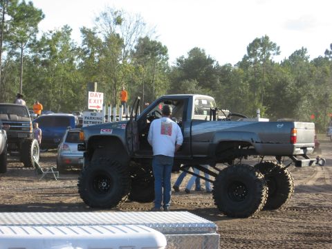 1994 Ford Bronco - A heavily modified pickup truck with oversized tires is parked outdoors with other vehicles and people present.