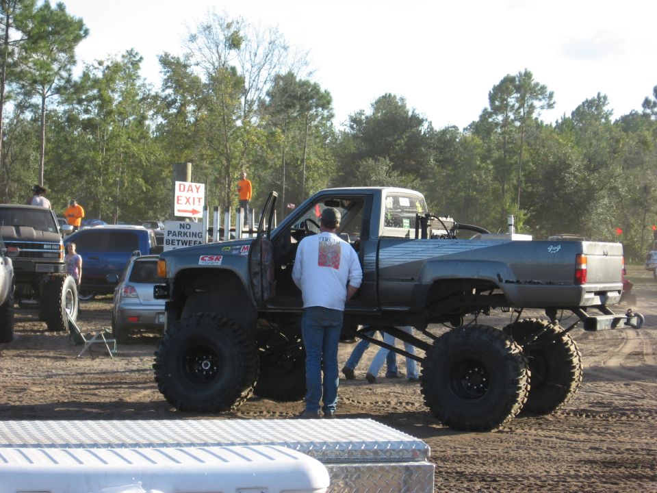 Lifted pickup truck with large tires, driver's door open, people around