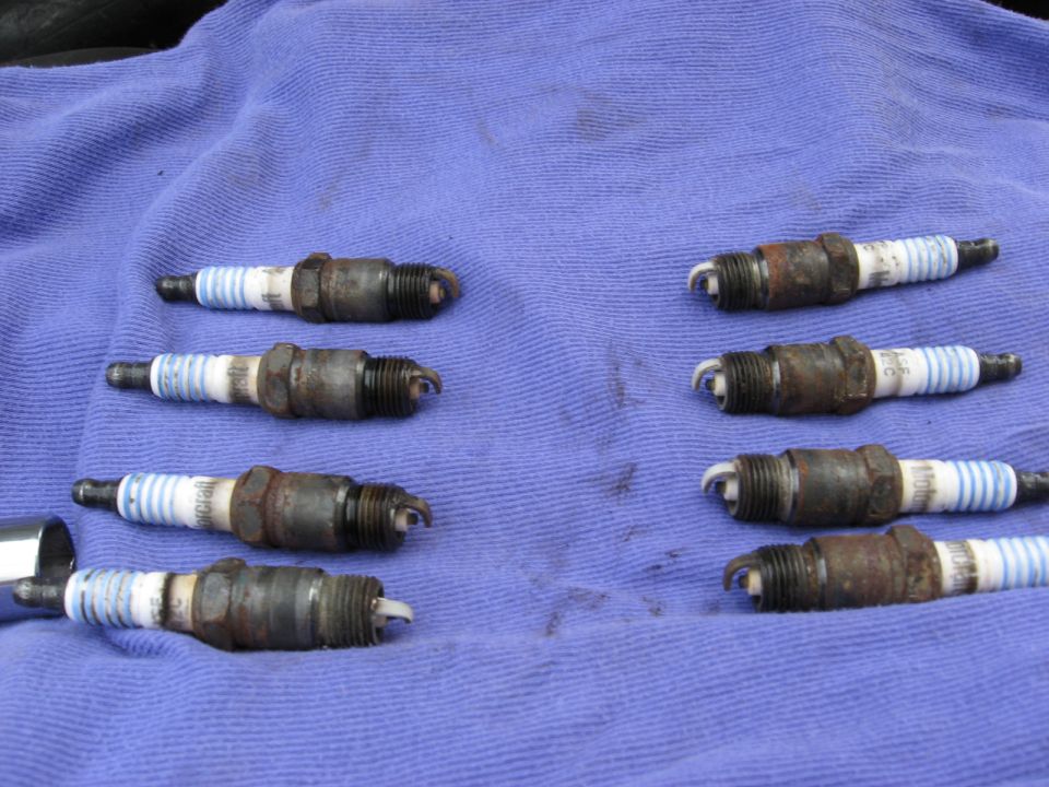Eight used spark plugs laid out on a blue cloth