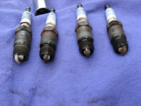 1994 Ford Bronco - Four used spark plugs are laid out on a blue cloth, with a socket wrench visible above.