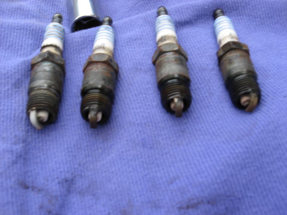 Four used spark plugs on a blue cloth with a socket wrench in the background