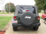 1995 Ford Bronco - Rear view of a green Jeep Wrangler parked in a driveway with a spare tire cover and a partial view of another vehicle.