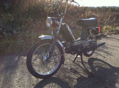 1981 Garelli Rally Sport - A green moped with chrome accents is parked on a paved surface, with a grassy embankment in the background.